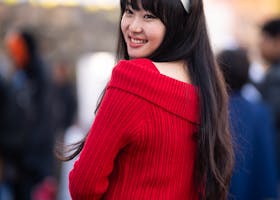Portrait of a smiling woman in a red sweater at a lively outdoor event in Kathmandu.